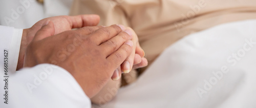 Closeup hands of doctor man encourage with elderly patient at the hospital, physician take care and holding hands for consoling senior sick, diagnostic disease and illness, medical concept.