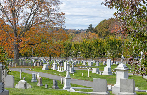Looking over the white and clean tombstones and gravestones in a cemetery during the day on a beautiful autumn day with peak fall foliage. The bright colors of the neat graveyard in Haverhill Mass.