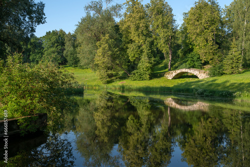 View of the Apollo Bridge on the bank of the Facade Pond on the Slavyanka River in Pavlovsky Park on a sunny summer day, Pavlovsk, St. Petersburg, Russia