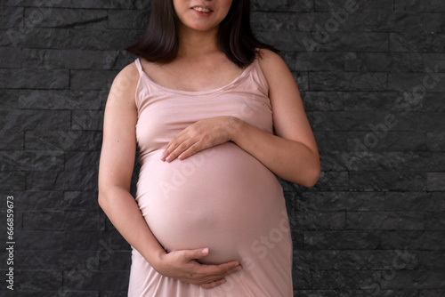 Mom pregnant woman in a dress holds hands on belly on black brick background, Waiting for the birth of your baby with love