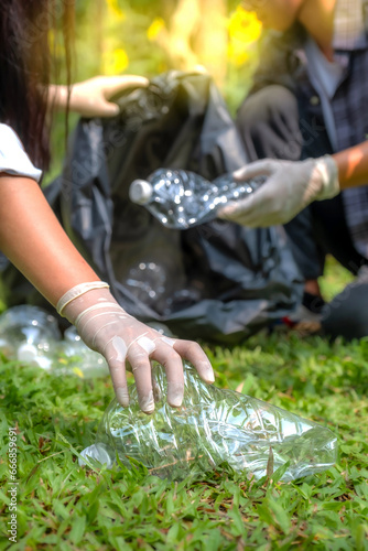 Hand holding plastic bottles waste, Couple picking up trash putting to the black garbage bag at Sunflower Park on Environmental Earth day
