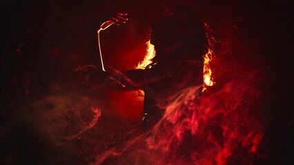 Fire dance. Body performance. Sensual artistic woman silhouette moving in red magic flame smoke in bright spot light on dark background copy space.