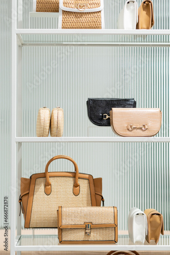 An assortment of shoes and handbags are seen displayed on a white shelving unit in a trendy retail store. Fluted glass can be seen behind the items.