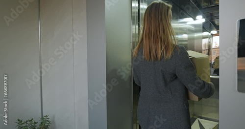 Happy woman with cardboard box entering into elevator