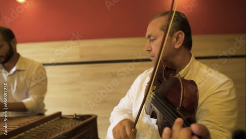 Roma Gypsies elderly members professional musicians playing together song music on violin and cimbalom inside a restaurant venue wearing white shirts being classy and respectful red wooden wall nice photo