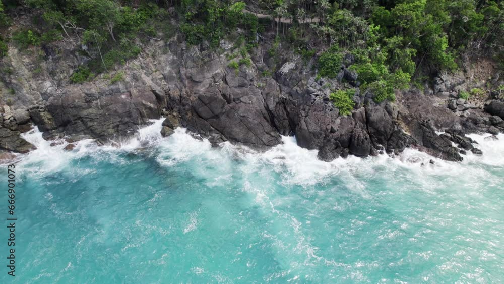 Serene aerial wide shot of water crashing on rocks by the beach shore sand blue sky white clouds turquoise water relaxation vacation tourism Serene aerial wide shot of water crashing on rocks by the beach shore sand blue sky white clouds turquoise water relaxation vacation tourism