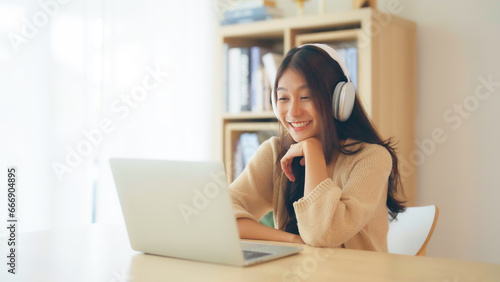 Young asian woman wearing headset while working on computer laptop at house. Work at home, Video conference, Video call, Student learning online class photo