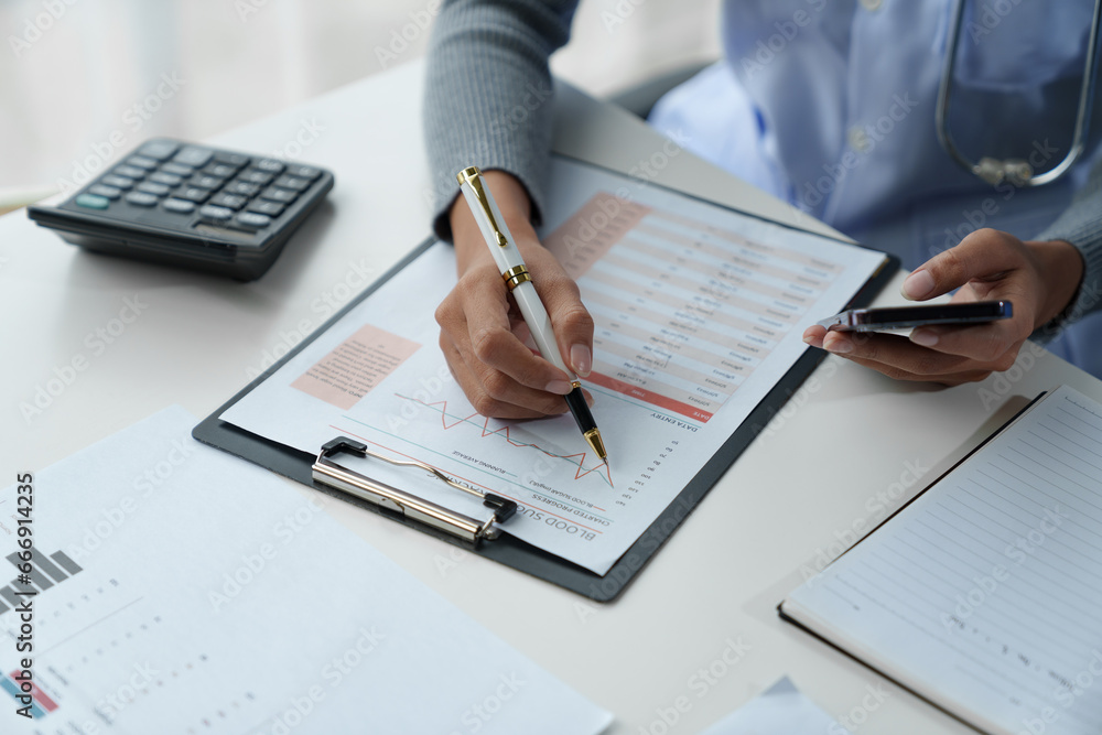 Fototapeta premium Confident female doctor, therapist sitting at table with medical stethoscope using laptop and mobile phone to write medical notes planning concept Study the treatment system Life insurance analysis.