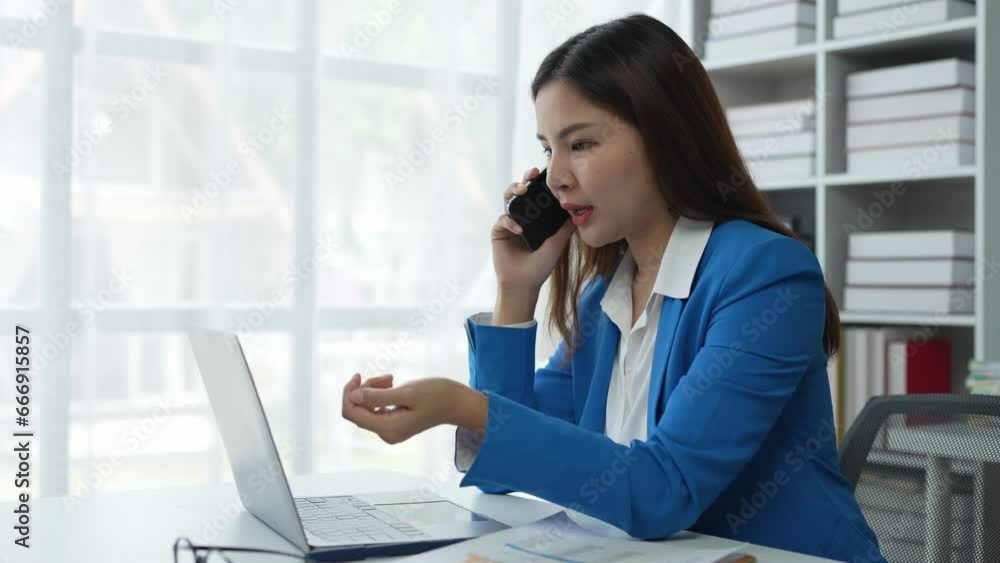 Asian businesswomen entrepreneurs are busy with their work in the office. Young Asian woman talking over a smartphone or cellphone while working on a computer at her desk. Asian businesswomen entrepreneurs are busy with their work in the office. Young Asian woman talking over a smartphone or cellphone while working on a computer at her desk.