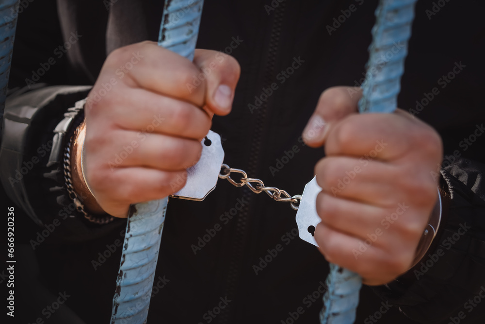 Handcuffed hands of a prisoner behind bars of a prison. concept of unfreedom. a handcuffed prisoner in a prison or courtroom. Handcuffed hands of a prisoner behind bars of a prison. concept of unfreedom. a handcuffed prisoner in a prison or courtroom.