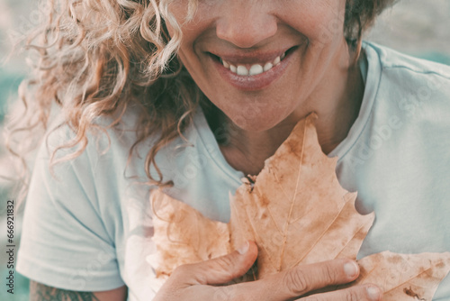 People love nature and feeling contact environment. One cheerful woman smile and hug to protect a big autumn yellow maple leaf on her chest. Concept of environment lifestyle. One adult female outdoor photo