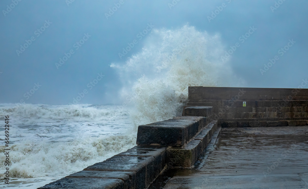 Storm hitting the coast of Scotland with crashing waves coming over a harbour wall