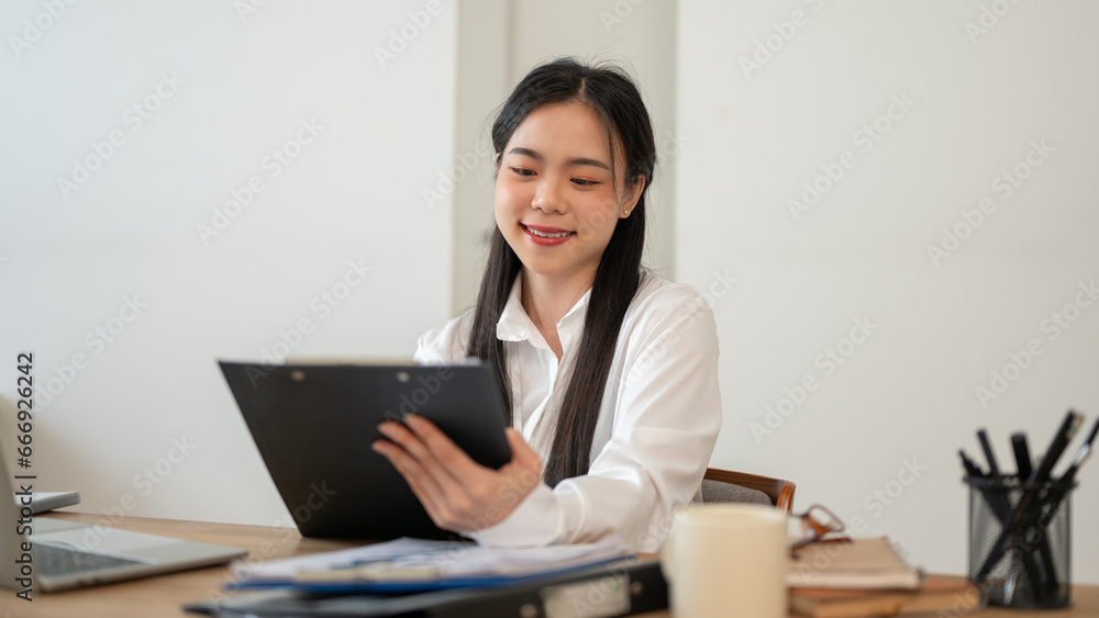 A charming Asian businesswoman is examining marketing report, working at her desk in her office. A charming Asian businesswoman is examining marketing report, working at her desk in her office.