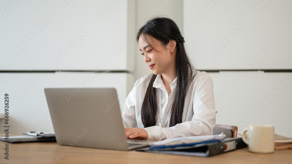 An attractive Asian businesswoman is working on her laptop at her desk in a modern office. An attractive Asian businesswoman is working on her laptop at her desk in a modern office.