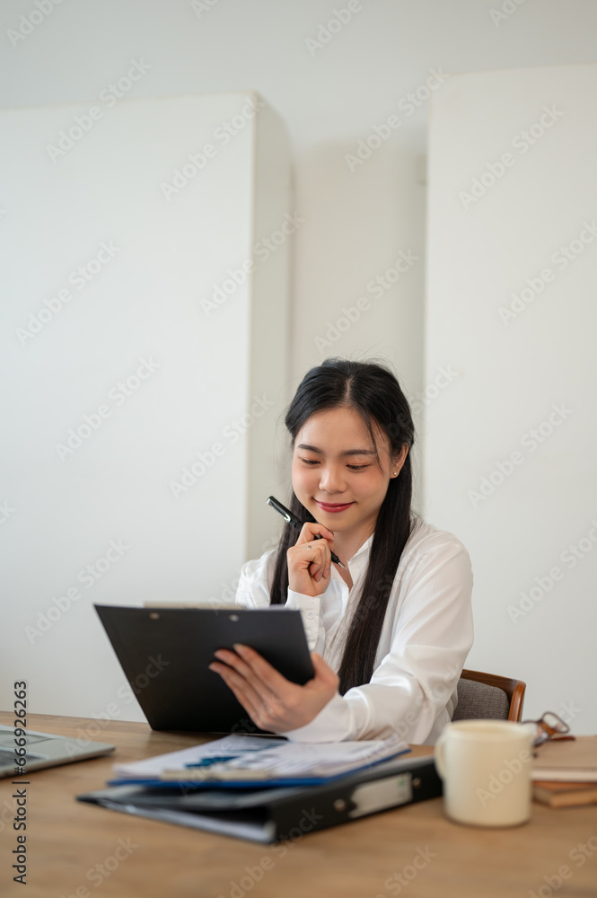 A beautiful Asian businesswoman is reviewing business report at her desk, working in her office. A beautiful Asian businesswoman is reviewing business report at her desk, working in her office.