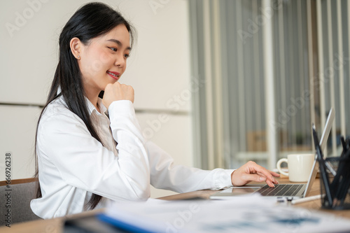 A beautiful Asian businesswoman or female office employee is working on her laptop at her desk.