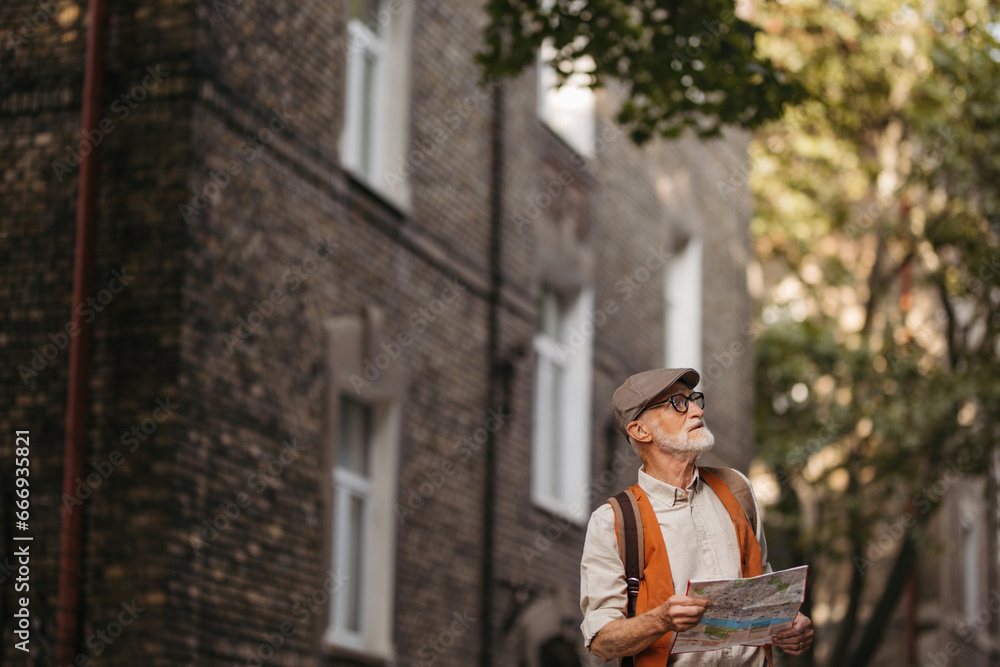 Senior tourist exploring a new city, exploring interesting places. Elderly man holding paper map, looking for the route. Traveling and trips in retirement.