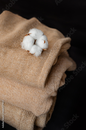 Folded knitted sweaters with cotton flowers on a black background.Autumn or winter season, sale.Stack of cashmere clothes. clothing made from natural materials.Close-up of knit texture.