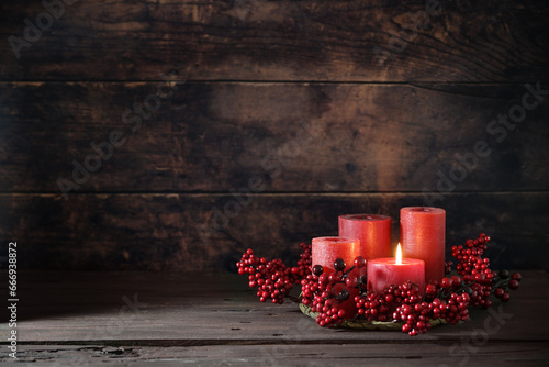 Frist Advent with red berry decoration and candles in a wreath, one is lighted, holiday home decor against a dark rustic wooden background, copy space, selected focus