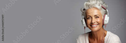Beautiful elderly happy woman with headphones on gray background. Banner. Copy space for text photo
