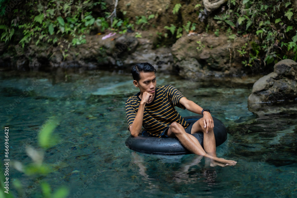A man enjoys a very clean spring river using a float tube. Located on the Udal Gumuk river, Magelang, Central Java, Indonesia. A man enjoys a very clean spring river using a float tube. Located on the Udal Gumuk river, Magelang, Central Java, Indonesia.