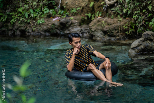 Fototapeta Naklejka Na Ścianę i Meble -  A man enjoys a very clean spring river using a float tube. Located on the Udal Gumuk river, Magelang, Central Java, Indonesia.