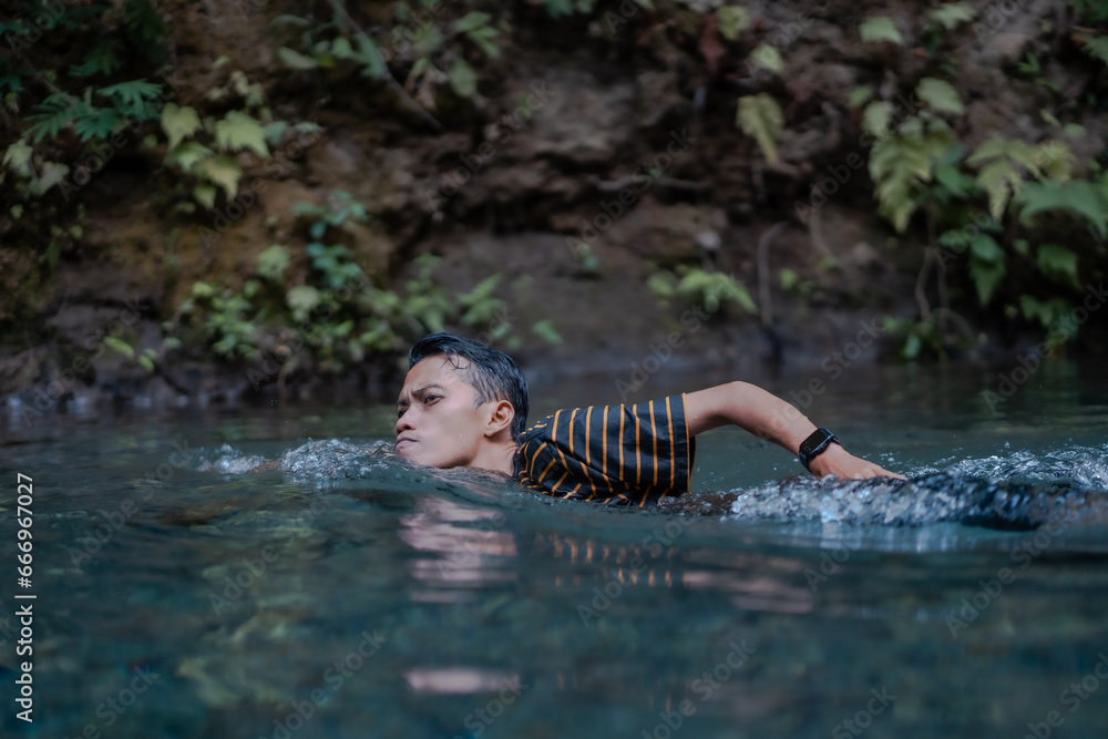 A man swimming in a very clean spring river. Located on the Udal Gumuk river, Magelang, Central Java, Indonesia.