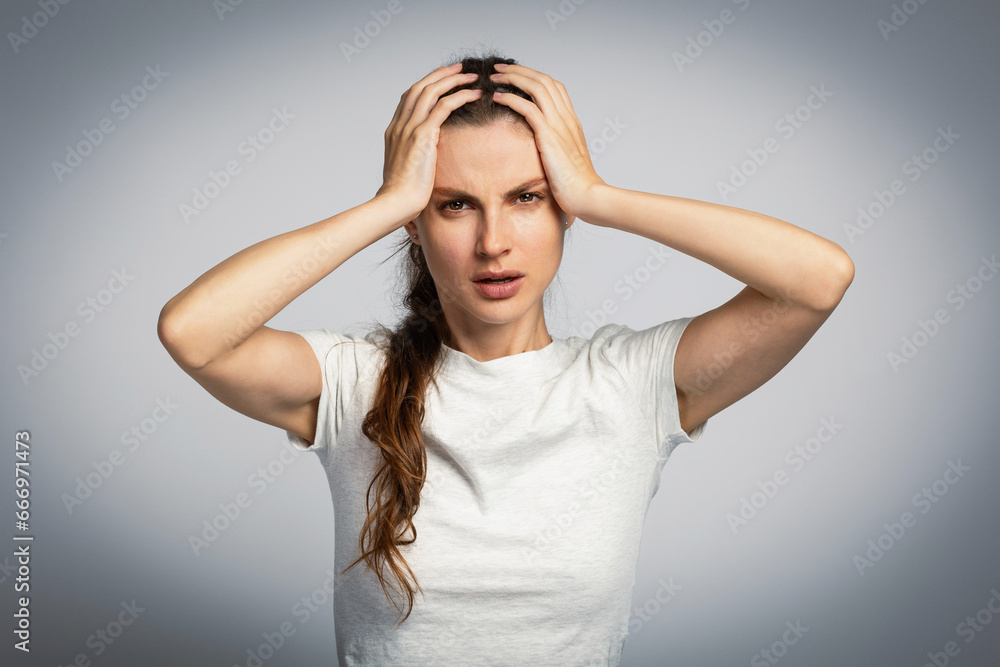 Young attractive girl in stress with headache or problems, holding her head in between her hands, on light grey studio background Young attractive girl in stress with headache or problems, holding her head in between her hands, on light grey studio background