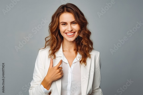 Portrait of handsome cheerful young businesswoman pointing at something. Professional young woman in a suit on grey background making hand gesture.