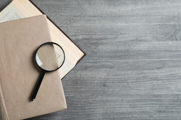 Magnifier on books on wooden table on light background, space for text