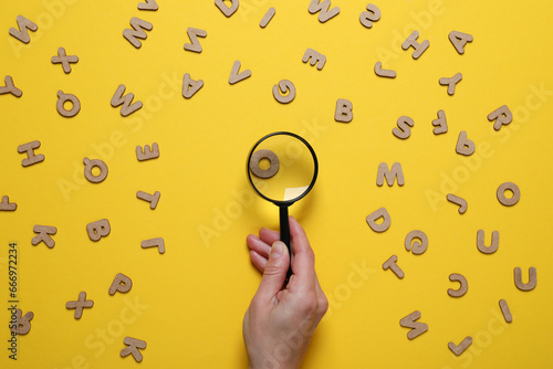 фотографія Magnifier in hand and letters on yellow background, top view