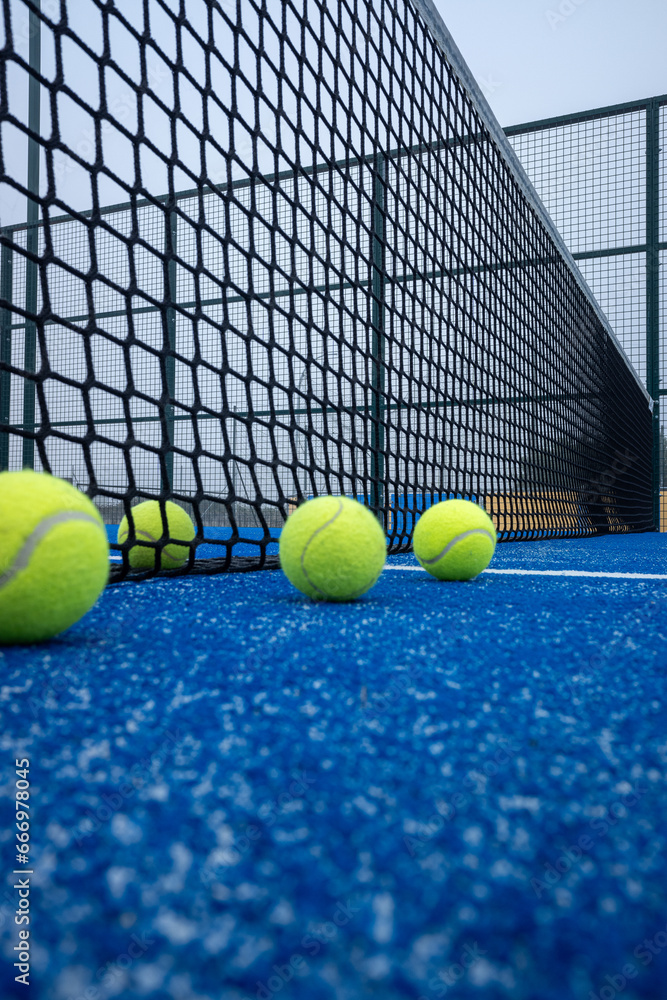 four paddle tennis balls next to the net on a blue artificial grass court