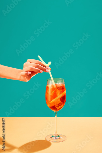 Konstfotografi Female hand putting straw into Aperol spritz cocktail isolated over green background
