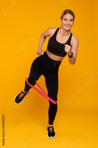 Woman exercising with elastic resistance band on orange background