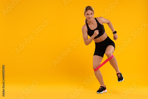 Woman exercising with elastic resistance band on orange background. Space for text