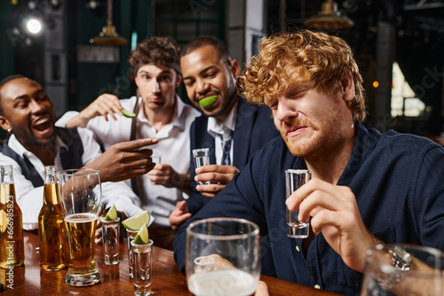Bilde på lerret focus on redhead man grimacing while drinking tequila shot near interracial frie