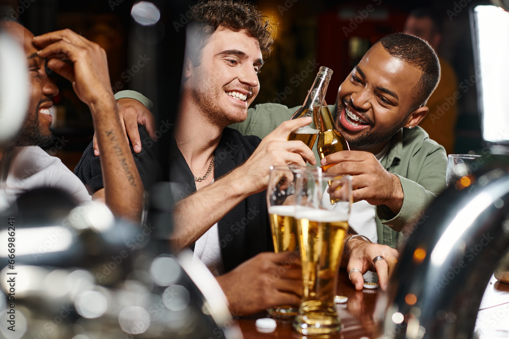 three interracial friends toasting with glasses of beer while spending time in bar, male friendship