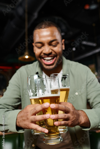 Wallpaper Mural cheerful african american man holding three glasses of beer in bar, having fun time during weekends Torontodigital.ca