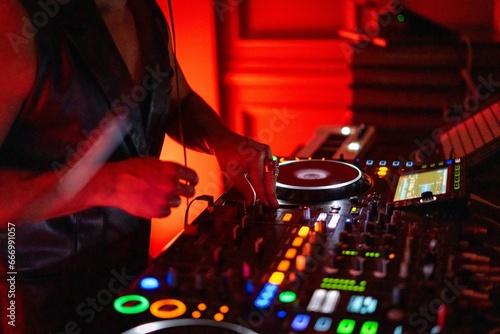DJ working on a professional controller in a dimly lit room, with illuminated buttons