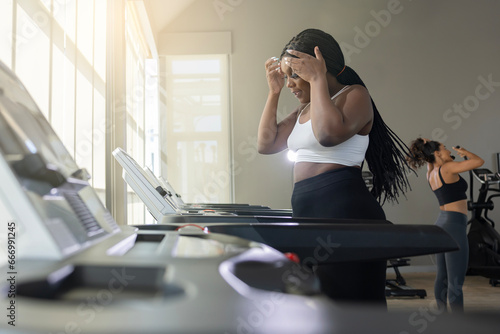 Stressful fat black woman worried about weight diet lifestyle while running on treadmill at gym.