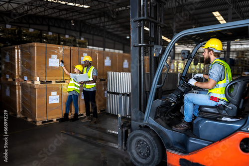 Factory worker man drive forklift operator in distribution warehouse with teammates working background 