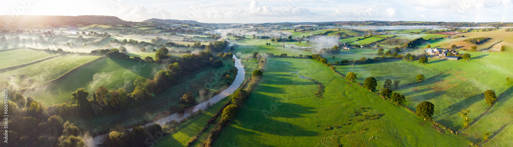 Aerial panorama picture of the river Otter near Honiton and Ottery St Mary. Sunrise and rolling mist cross the lush green fields below. Spectacular landscape. 
