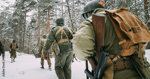 Obraz na płótnie Heroes Of War. Re-enactors Dressed As American Infantry Soldier Marching Through Forest Road In Cold Winter Day. Group Of Usa Soldiers Marching Country Road. Usa Army Soldiers Of World War Ii. w salonie