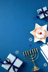 Hanukkah Jewish holiday vertical background with gold menorah, gift boxes, candles, traditional donut with jam on blue table. Flat lay, top view.