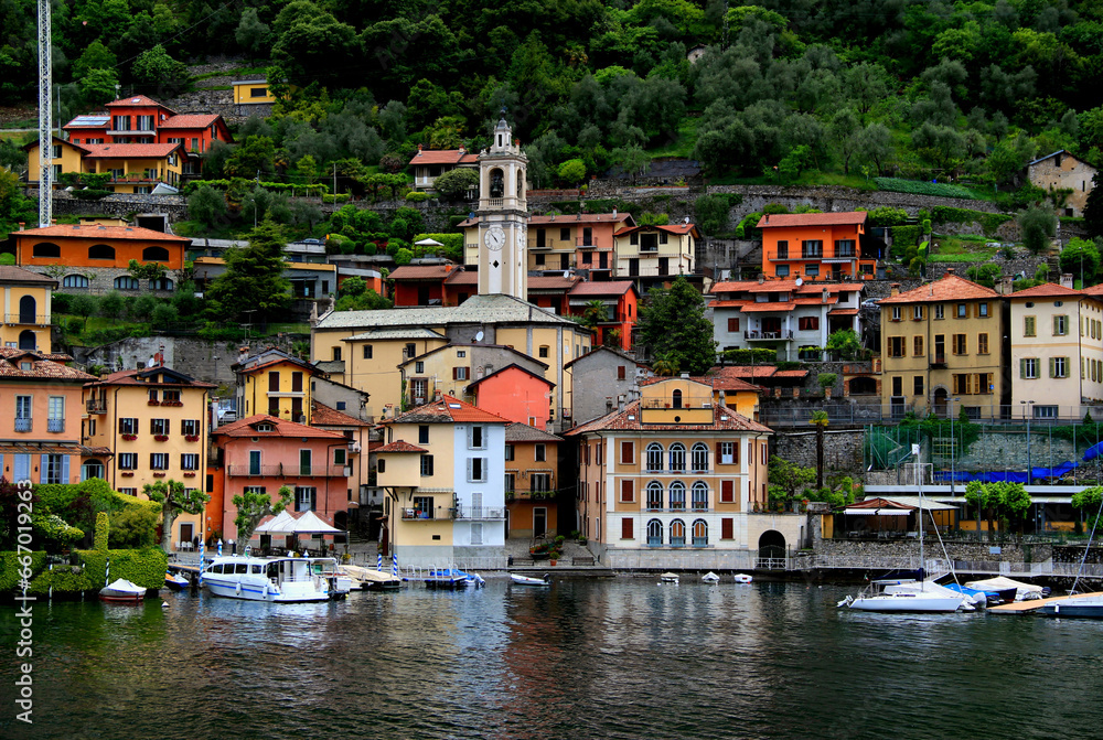 Landscape view of one of the many small towns on Lake Como with a church and numerous boats in the foreground and houses on a hillside during the rain in northern Italy