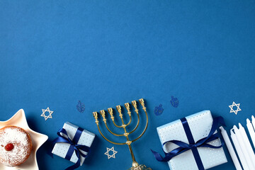 Jewish holiday Hanukkah concept. Flat lay gold menorah, traditional jelly donut, gift boxes, candles, confetti on blue background.