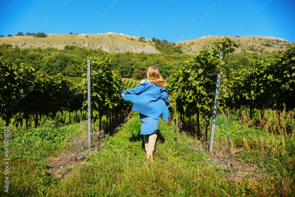 A long-haired girl running through a vineyard on a sunny summer day