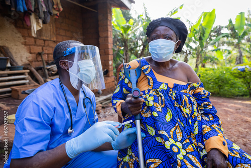 Young African doctor prepares to inject a dose of vaccine into a sick old woman