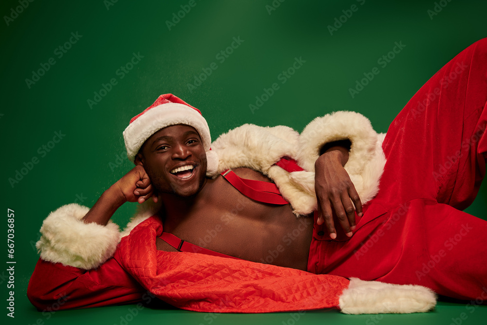 african american man with radiant smile lying down in santa costume on shirtless body on green african american man with radiant smile lying down in santa costume on shirtless body on green