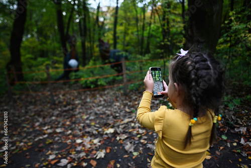 Little girl photographing autumn forest with a smartphone in the park.